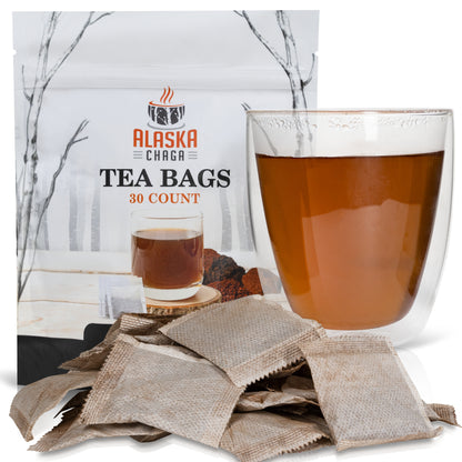 Alaska Chaga Tea Bags pouch beside a glass mug of brewed chaga tea with loose tea bags in front